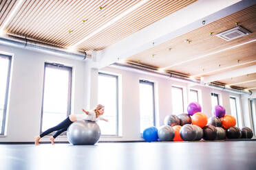 Junge schöne Frau bei einer Übung mit einem Fitball in einem Fitnessstudio. - HPIF22670