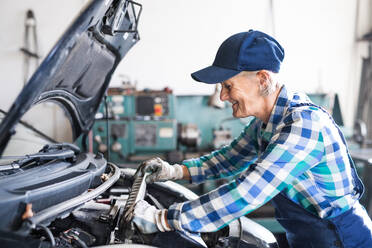 Eine ältere Frau arbeitet in einer Werkstatt und repariert ein Auto. - HPIF22739