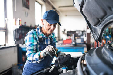 Eine ältere Frau arbeitet in einer Werkstatt und repariert ein Auto. - HPIF22740