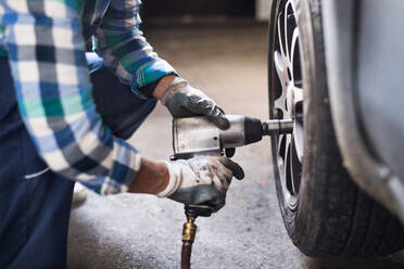 Mechanikerin bei der Reparatur eines Autos. Eine nicht erkennbare Frau arbeitet in einer Werkstatt. - HPIF22743