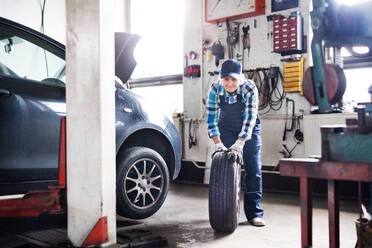 Eine ältere Frau arbeitet in einer Werkstatt und repariert ein Auto. - HPIF22745