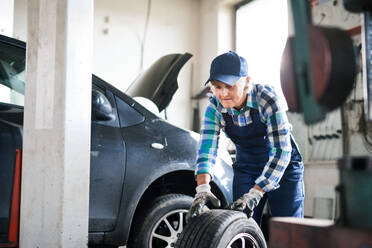 Eine ältere Frau arbeitet in einer Werkstatt und repariert ein Auto. - HPIF22746