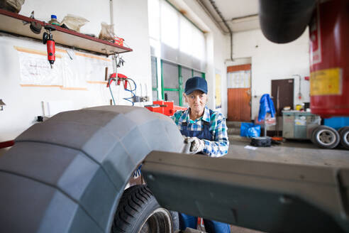 Eine ältere Frau arbeitet in einer Werkstatt und repariert ein Auto. - HPIF22759