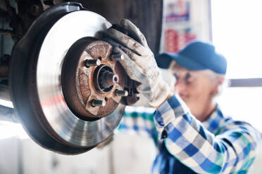 Eine ältere Frau arbeitet in einer Werkstatt und repariert ein Auto. - HPIF22763