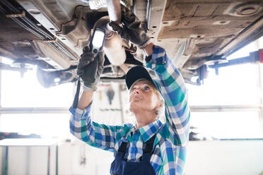 Eine ältere Frau arbeitet in einer Werkstatt und repariert ein Auto. - HPIF22766