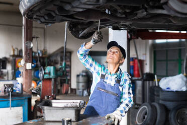 Eine ältere Frau arbeitet in einer Werkstatt und repariert ein Auto. - HPIF22769