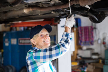 Eine ältere Frau arbeitet in einer Werkstatt und repariert ein Auto. - HPIF22770