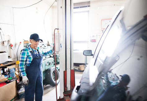 Eine Frau repariert ein Auto, eine ältere Frau steht in einer Werkstatt. - HPIF22774