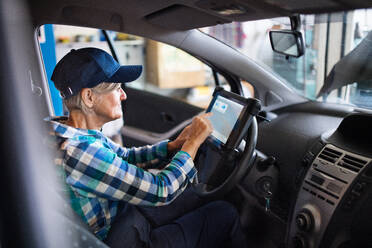 Eine ältere Frau arbeitet in einer Werkstatt und repariert ein Auto. - HPIF22780