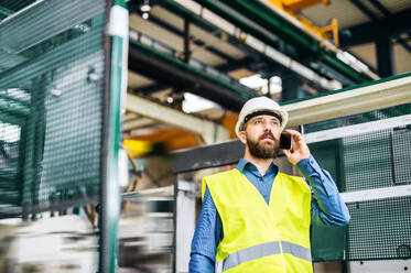 A portrait of a mature industrial man engineer with smartphone working in a factory, making a phone call. - HPIF22786