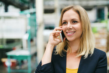 Das Porträt einer glücklichen Ingenieurin, die in einer Fabrik steht und telefoniert. - HPIF22788