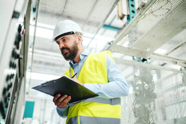 A portrait of a mature industrial man engineer with clipboard in a factory, working. Copy space. - HPIF22794