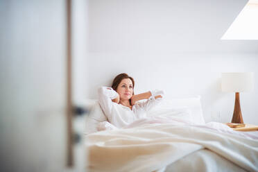 A happy young woman sitting in bed indoors in the morning in a bedroom, resting. - HPIF22815