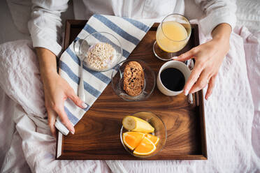 A midsection of woman lying in bed with coffee and breakfast indoors in the morning in a bedroom. A top view. - HPIF22817