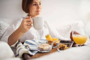 A young woman lying in bed with coffee and breakfast indoors in the morning in a bedroom. - HPIF22822