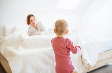 Eine glückliche junge Mutter mit ihrer kleinen Tochter, die am Morgen im Bett liegt und spielt. - HPIF22823