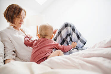 Eine glückliche junge Mutter mit ihrer kleinen Tochter, die am Morgen im Haus auf dem Bett sitzt und spielt. - HPIF22825