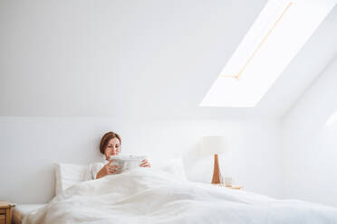 Morgenroutine einer jungen Frau, die im Bett in einem Schlafzimmer Zeitung liest. - HPIF22846