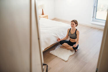 Blick aus der Vogelperspektive auf eine junge Frau, die in einem Schlafzimmer Yoga-Übungen macht. Kopierraum. - HPIF22861