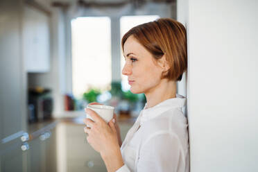 Eine junge, zufriedene Frau mit einer Tasse Kaffee, die in einem Haus steht und sich an eine Wand lehnt; Raum kopieren. - HPIF22888