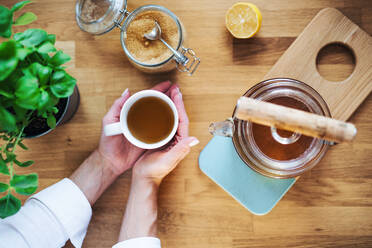 Eine Komposition von Frauenhänden, die eine Tasse Tee, eine Teekanne und Zucker auf einem Holztisch halten, von oben gesehen. - HPIF22897