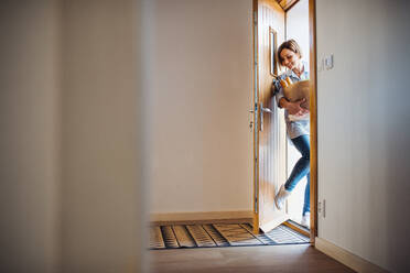Eine junge Frau mit Lebensmitteln in einer Papiertragetasche geht durch die Eingangstür ihres Hauses. - HPIF22901
