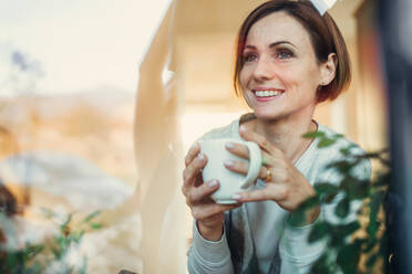 Eine junge Frau mit einer Tasse Kaffee, die aus einem Fenster schaut, aufgenommen durch Glas, ein Kopierraum. - HPIF22909