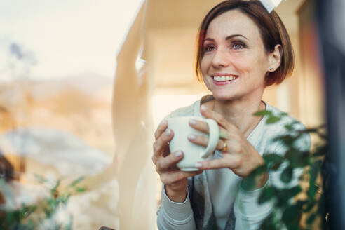 A young woman with cup of coffee looking out of a window. Shot through glass. A copy space. - HPIF22909