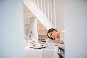 Eine müde junge Frau, die in einem Haus sitzt und im Home Office arbeitet. - HPIF22924