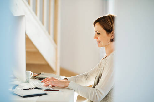 Eine glückliche junge Frau, die in einem Haus sitzt und im Home Office arbeitet. - HPIF22925