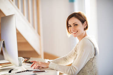 Eine glückliche junge Frau, die in einem Haus sitzt und im Home Office arbeitet. - HPIF22926