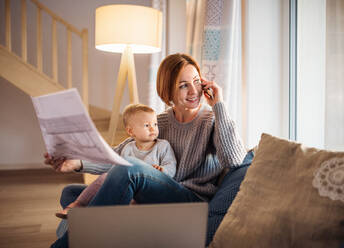 A young woman on the phone with a toddler daughter sitting indoors, working at home. - HPIF22940