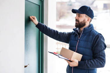 Ein Mann liefert ein Paket an den Empfänger aus - Kurierdienstkonzept. Ein Mann klopft an die Tür. - HPIF22949