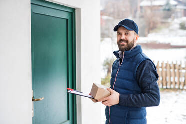 Delivery man delivering parcel box to recipient - courier service concept. A man standing by the door. - HPIF22950