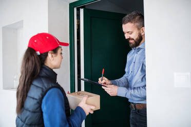 Ein Mann, der ein Paket von einer Zustellerin an der Tür erhält - Kurierdienstkonzept. - HPIF22954