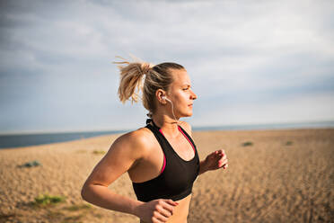 Junge sportliche Läuferin mit Kopfhörern, die draußen am Strand in der Natur läuft und Musik hört. - HPIF22978