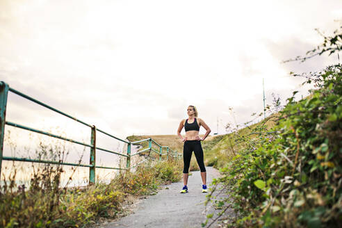 Junge sportliche Läuferin in schwarzer Sportkleidung, die draußen in der Natur steht und sich ausruht. Kopierraum. - HPIF22980
