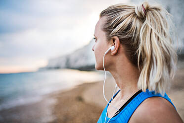 Junge sportliche Läuferin mit Kopfhörern, die draußen am Strand in der Natur steht, Musik hört und sich ausruht. Raum kopieren. - HPIF22981