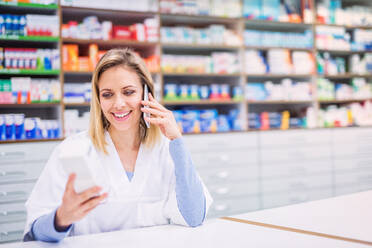 Young beautiful friendly female pharmacist with a smartphone, making a phone call. - HPIF22986