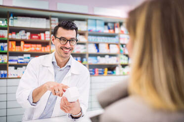 Handsome male friendly pharmacist serving an unrecognizable female customer. - HPIF22997
