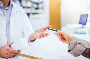 Unrecognizable male pharmacist serving a female customer. Credit or debit card payment. - HPIF22998