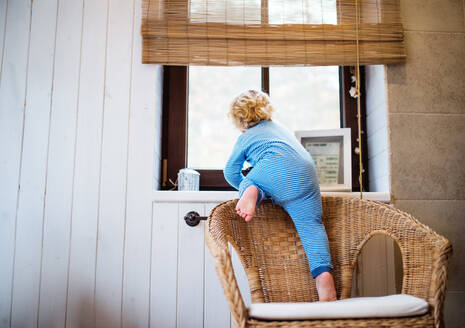 Kleines Kleinkind klettert auf ein Fensterbrett. Häuslicher Unfall. Gefährliche Situation zu Hause. Rückansicht. - HPIF23046