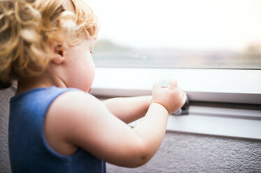 Kleines Kleinkind versucht, ein Fenster zu öffnen. Häuslicher Unfall. Gefährliche Situation zu Hause. Nahaufnahme. - HPIF23058