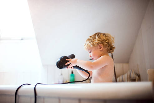 Niedlicher kleiner Junge mit einem Haartrockner in der Badewanne im Badezimmer. Gefährliche Situation. Häuslicher Unfall. - HPIF23063