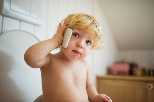 Niedliches Kleinkind mit einem Smartphone im Badezimmer. Kleiner Junge sitzt auf der Toilette. - HPIF23066