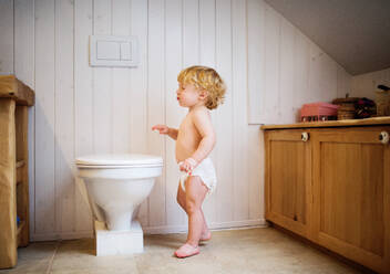 Niedliches Kleinkind im Badezimmer. Kleiner Junge steht auf der Toilette. - HPIF23068