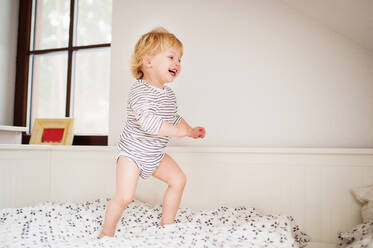 Niedliches Kleinkind, das auf dem Bett im Schlafzimmer springt. - HPIF23107