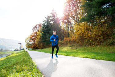 Junger Sportler in blauer Jacke, der draußen in der bunten, sonnigen Herbstnatur läuft. Trailrunner trainiert für den Crosslauf. - HPIF23138