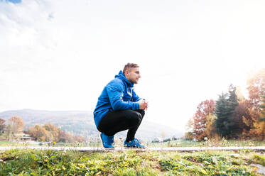 Junge Läuferin in blauer Jacke draußen in der bunten, sonnigen Herbstnatur auf einem Asphaltweg ruhend. Trailrunnerin trainiert für Langlauf. - HPIF23142