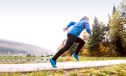 Junger Sportler in blauer Sportjacke am See beim Laufen gegen die bunte Herbstnatur. - HPIF23145